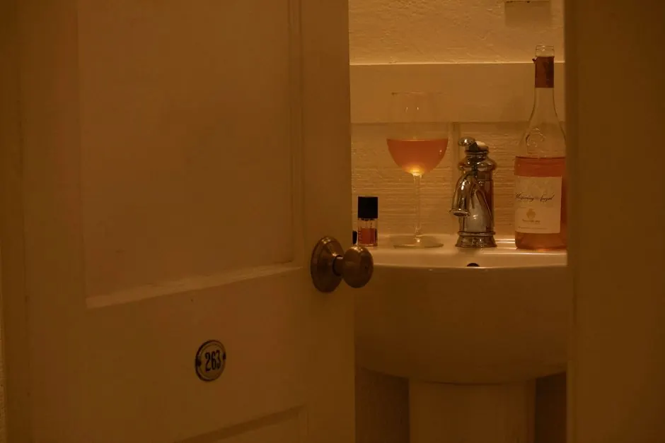 Warm lit bathroom with a rosé wine glass on sink, behind an open door.